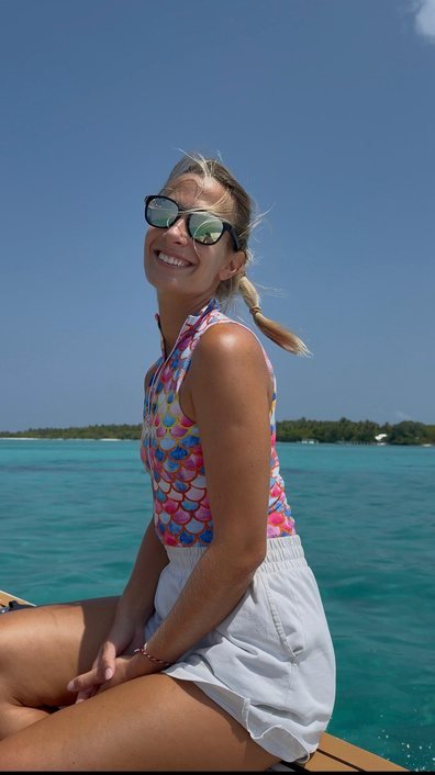 Ena on a boat in the Maldives, sea and low islands behind her