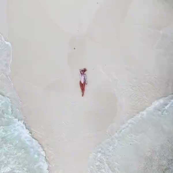 Aerial of a woman lying on the white sand as the waves wash in