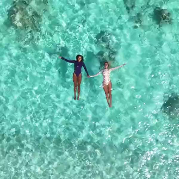 Two people floating side by side in turquoise shallows, seen from above