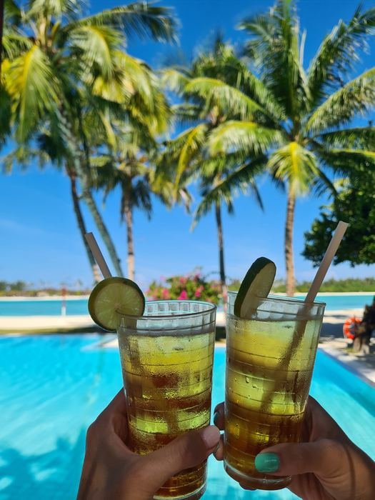 Two cold drinks raised by the pool under palm trees