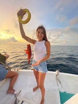 Woman on a boat at golden hour holding up a hat