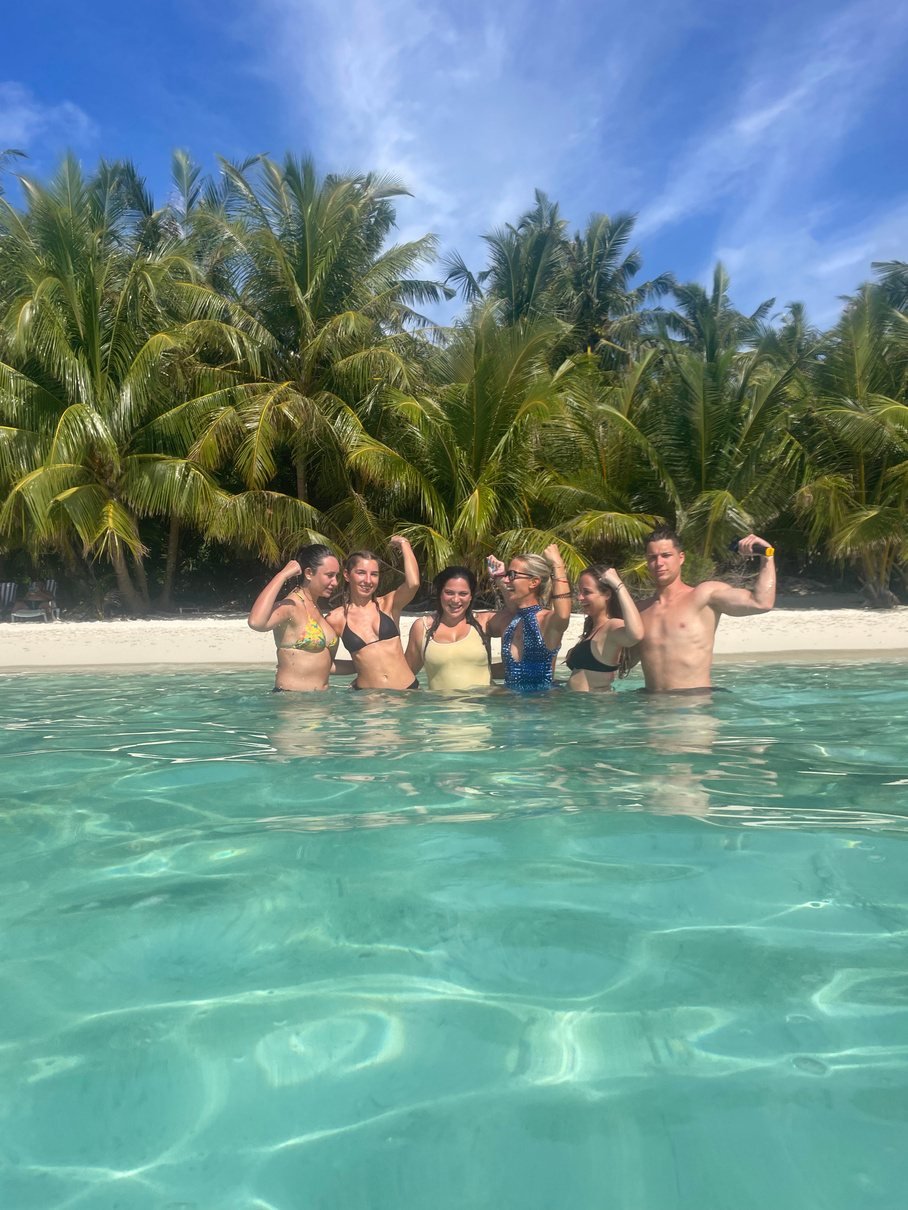 A group standing in turquoise shallows in front of palm trees